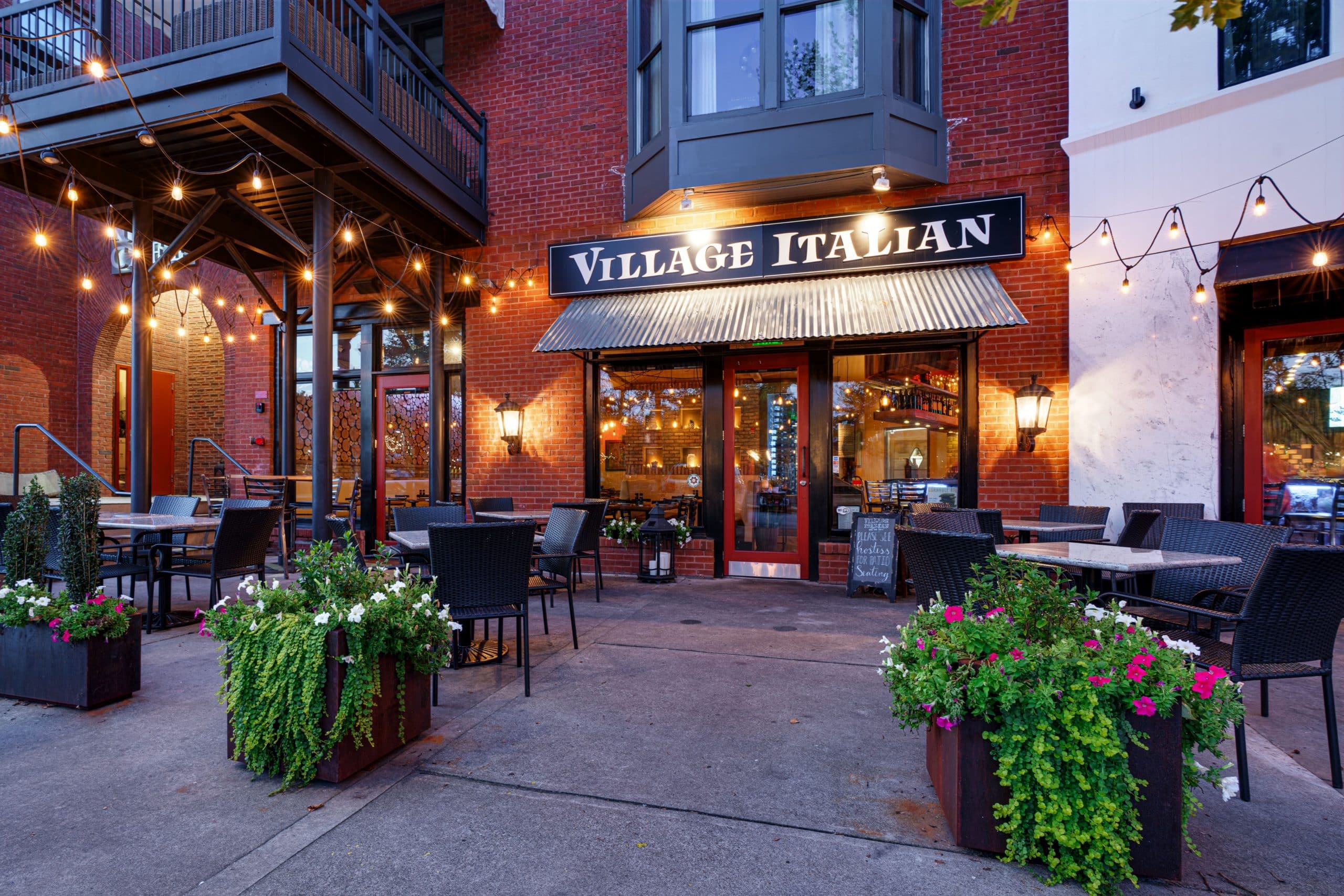 Exterior view of Village Italian restaurant with string lights and outdoor seating.