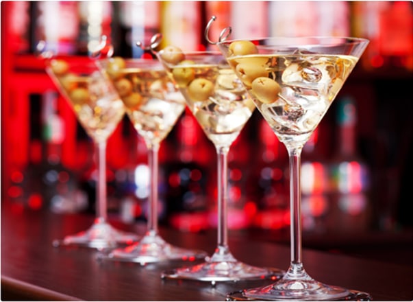 Four martini's lined up on a bar top garnished with olives